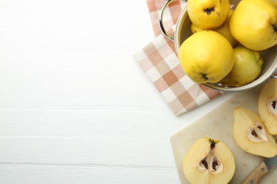 Photo of Tasty ripe quinces, metal colander and knife on white wooden table, flat lay. Space for text
