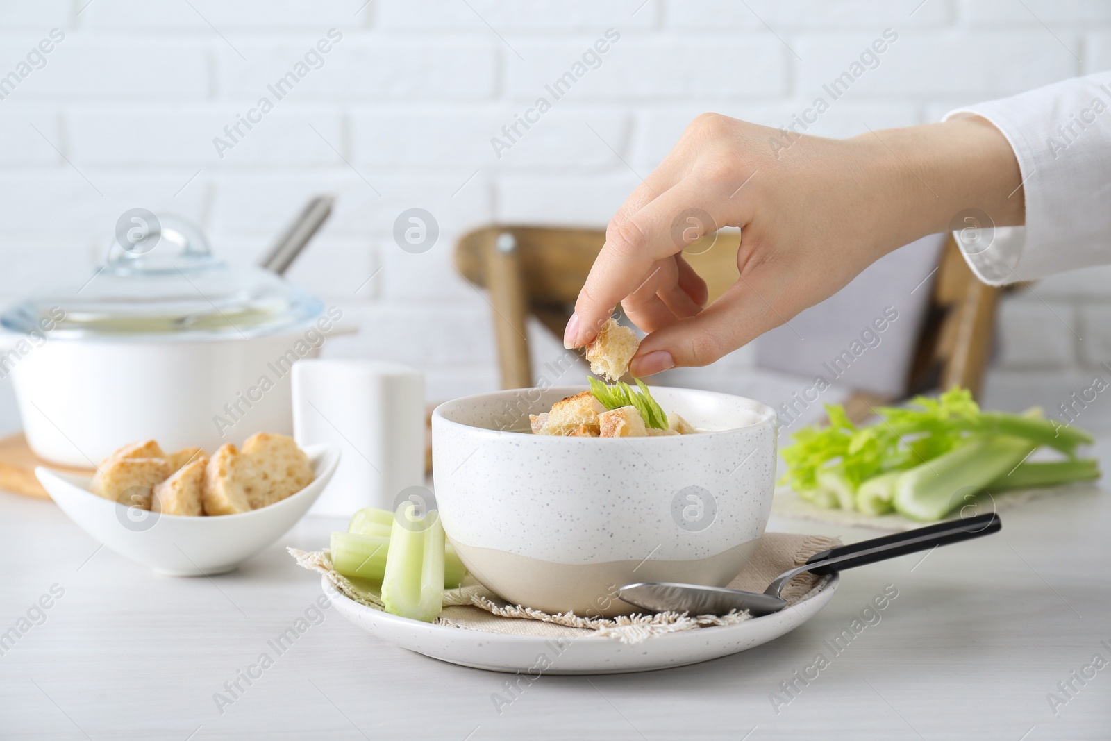 Photo of Woman decorating delicious celery soup at white table, closeup