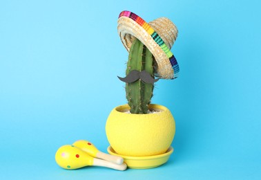 Photo of Mexican sombrero hat, cactus with fake mustache and maracas on light blue background
