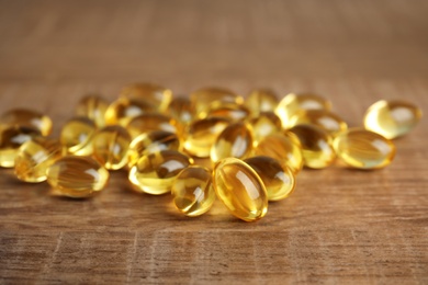 Photo of Cod liver oil pills on wooden background, closeup
