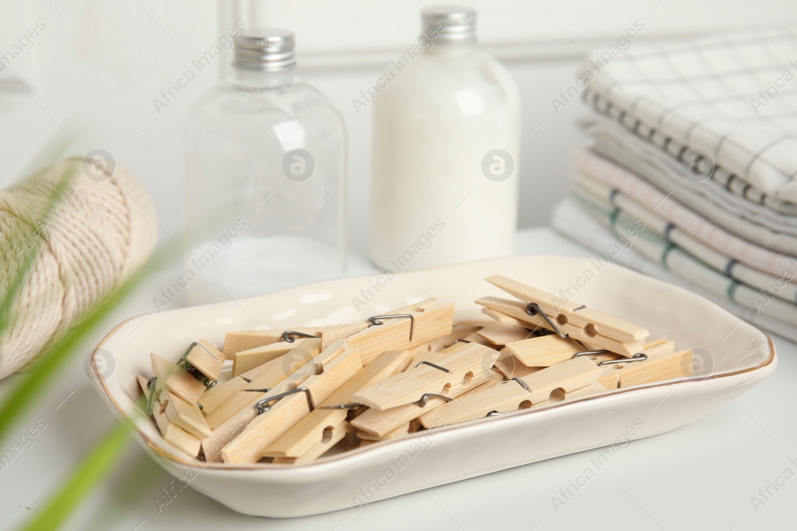 Photo of Many wooden clothespins in bowl on white table