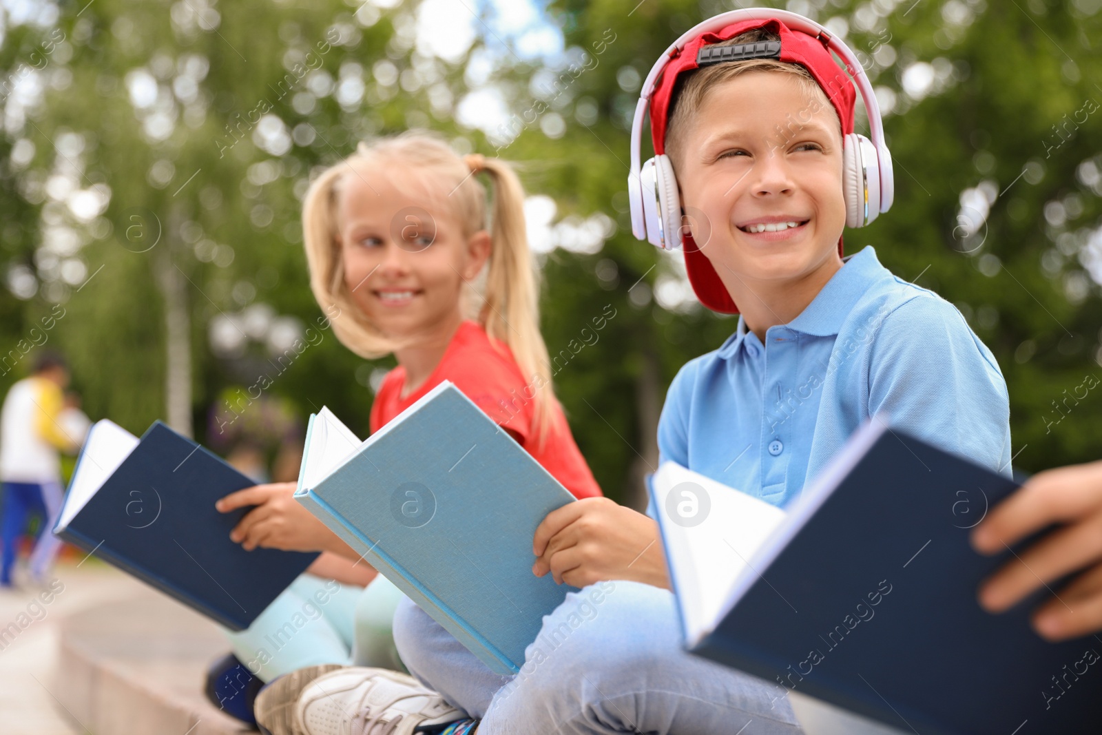 Photo of Cute boy in headphones and girl reading books in green park