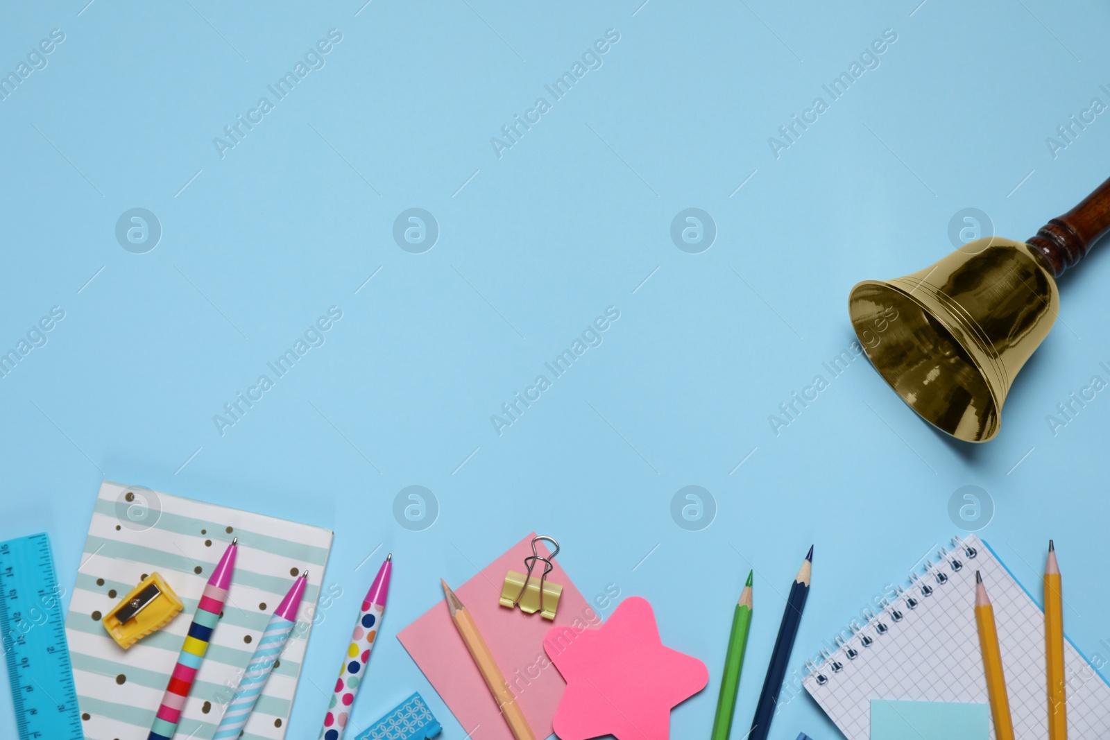 Photo of Different stationery and school bell on light blue background, flat lay. Space for text