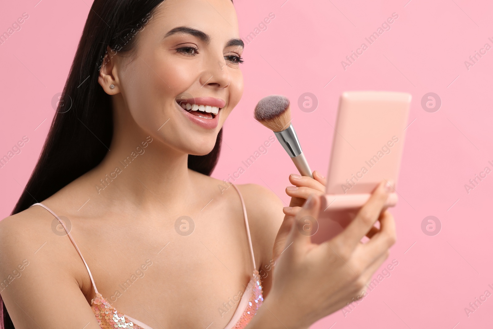 Photo of Beautiful woman with cosmetic pocket mirror applying makeup on pink background