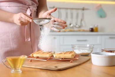 Woman decorating delicious Belgian waffles with powdered sugar at wooden table in kitchen, closeup