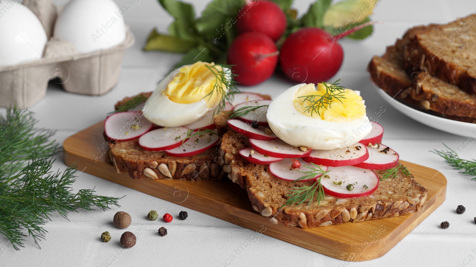Photo of Tasty sandwiches with boiled egg, radish and ingredients on white tiled table