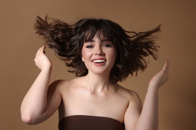 Portrait of beautiful young woman with wavy hairstyle on brown background
