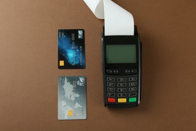 New modern payment terminal and credit cards on brown background, flat lay