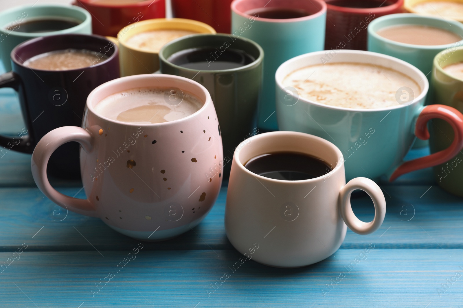 Photo of Many cups of different coffee drinks on light blue wooden table