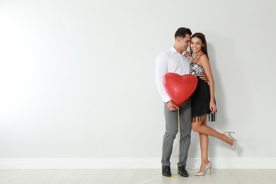 Photo of Beautiful couple with heart shaped balloon near light wall, space for text