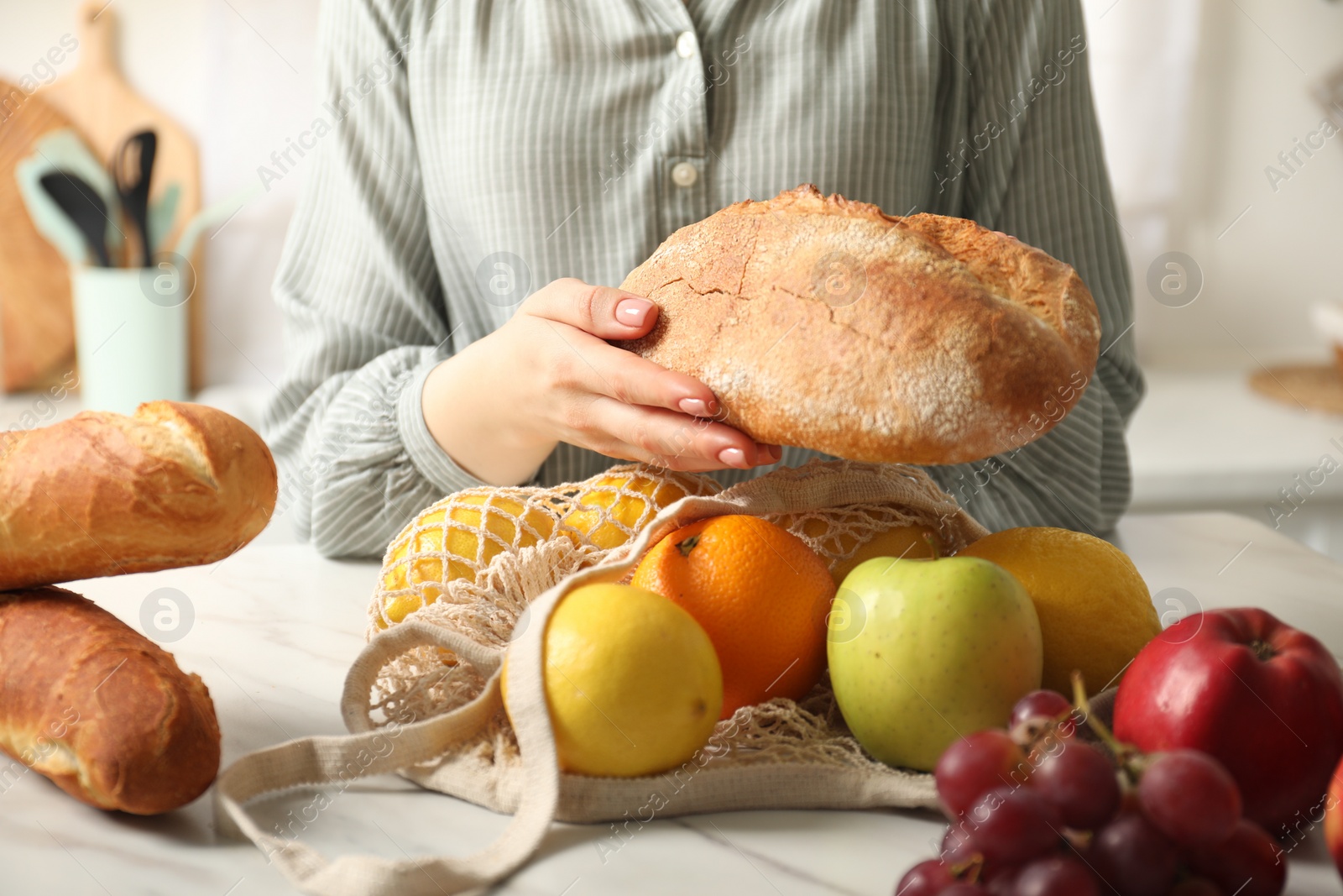 Photo of Woman bread and string bag of fresh fruits at light marble table, closeup