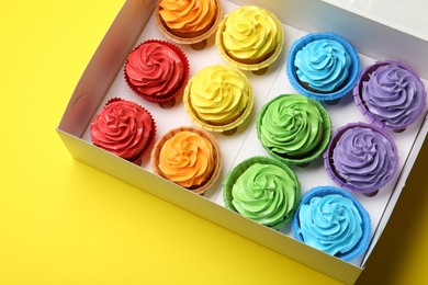 Photo of Tasty cupcakes in box on yellow background, above view