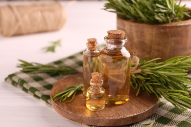 Essential oil in bottles and rosemary on white wooden table