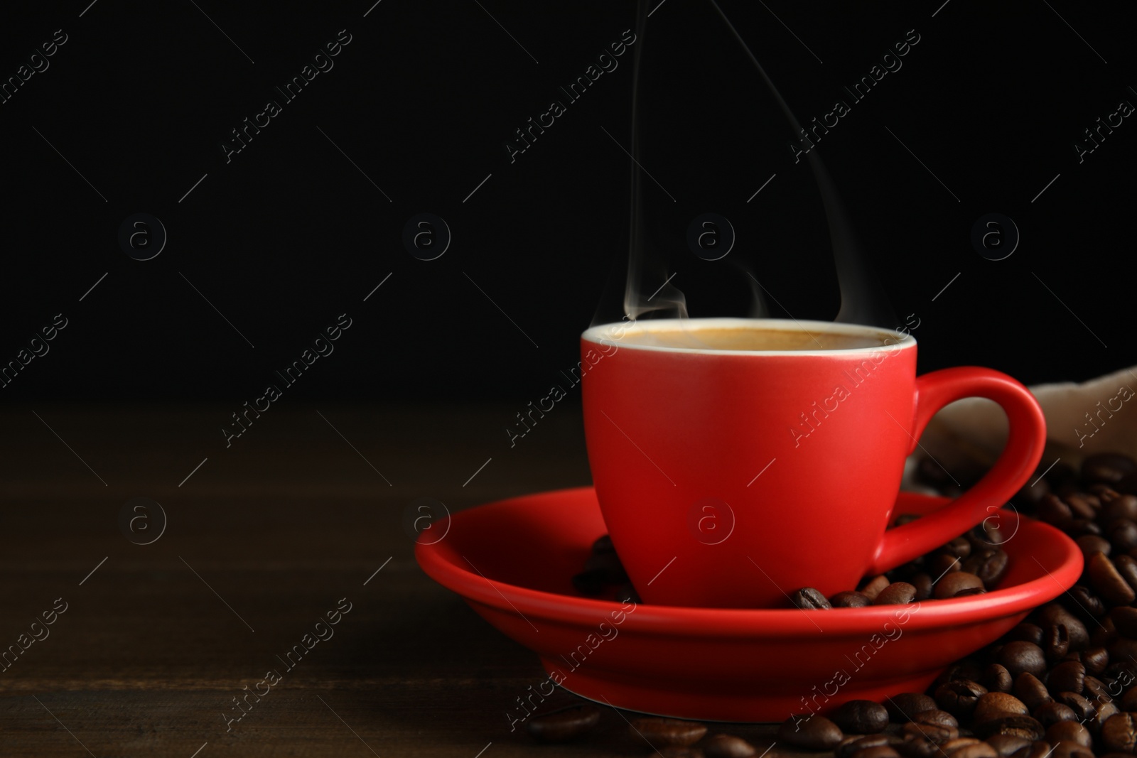 Photo of Cup of tasty coffee and beans on wooden table, space for text