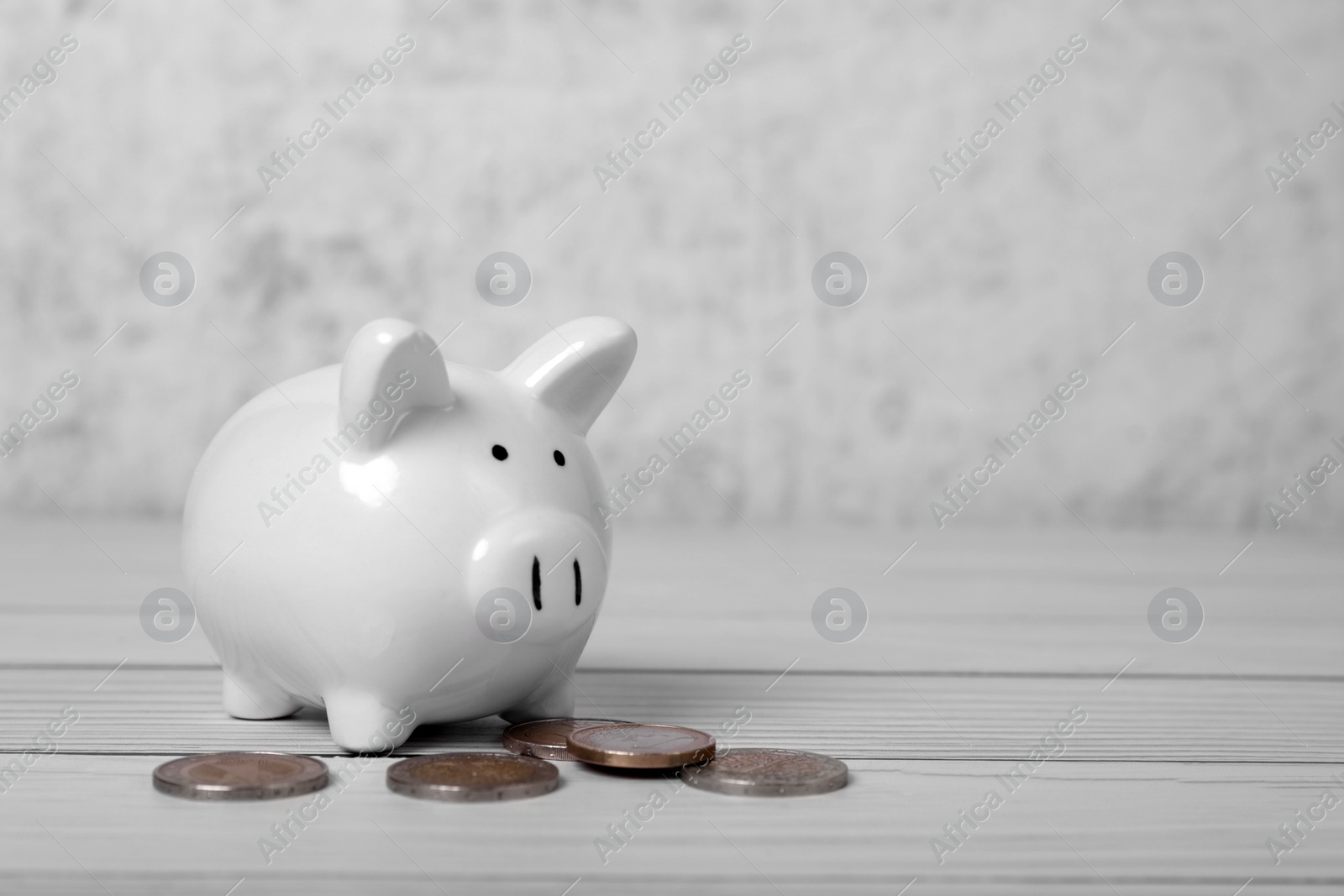 Photo of Ceramic piggy bank and coins on white wooden table, space for text. Financial savings