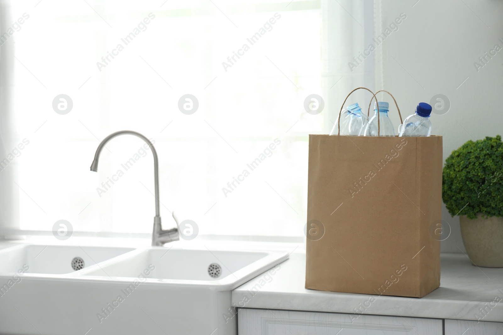 Photo of Paper bag with used plastic bottles on kitchen counter, space for text. Recycling problem