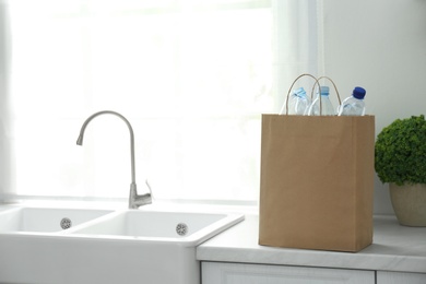 Photo of Paper bag with used plastic bottles on kitchen counter, space for text. Recycling problem