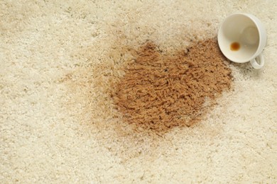 Photo of Overturned cup and spilled coffee on beige carpet, top view. Space for text