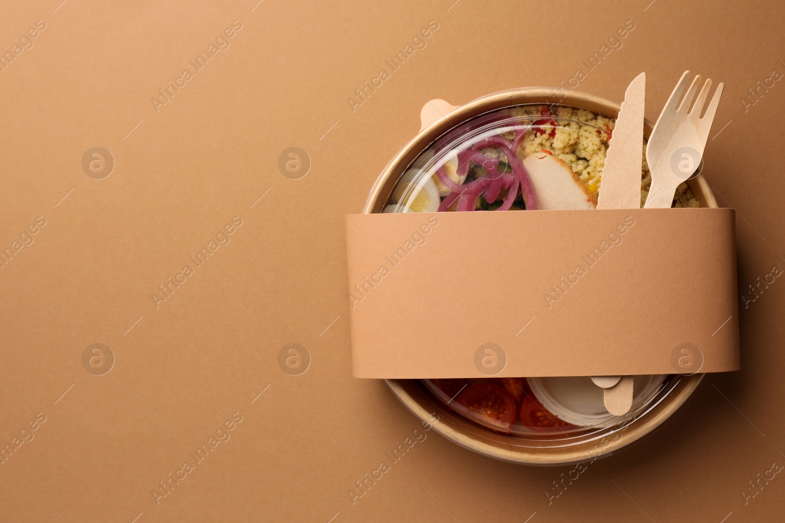 Photo of Tasty food in container with wooden fork and knife on beige background, top view. Space for text