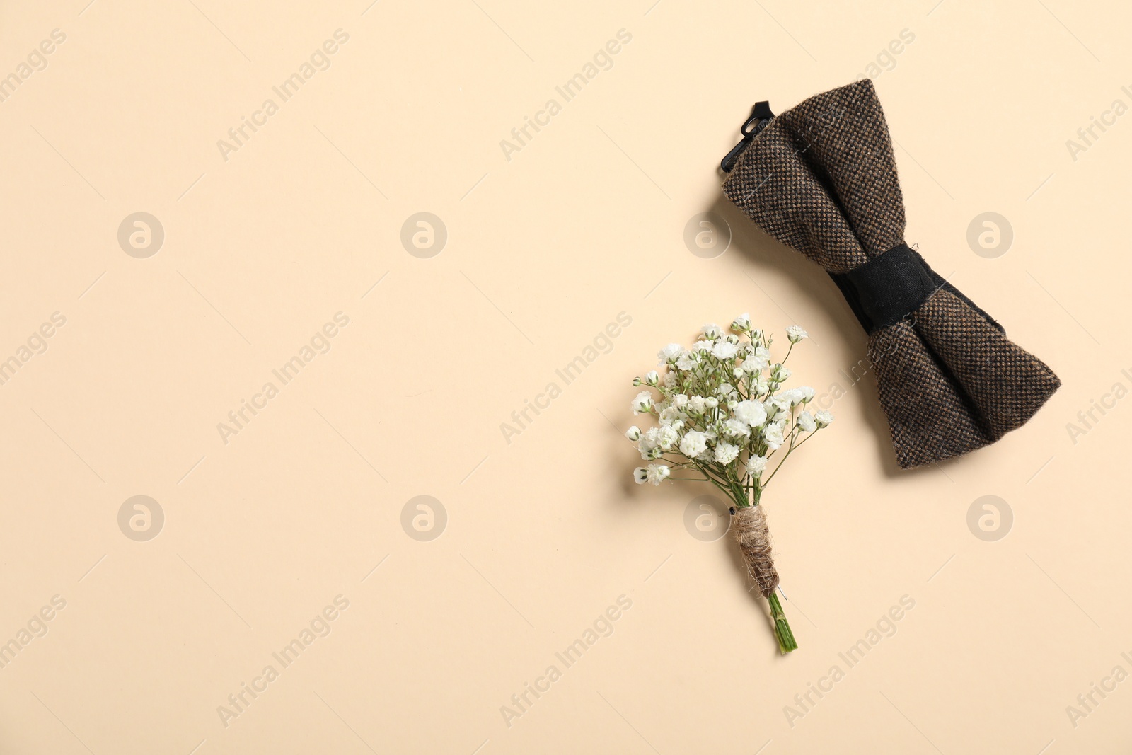 Photo of Wedding stuff. Stylish boutonniere and bow tie on beige background, top view. Space for text