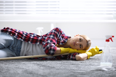Lazy young woman with mop lying on floor at home. Cleaning and housework