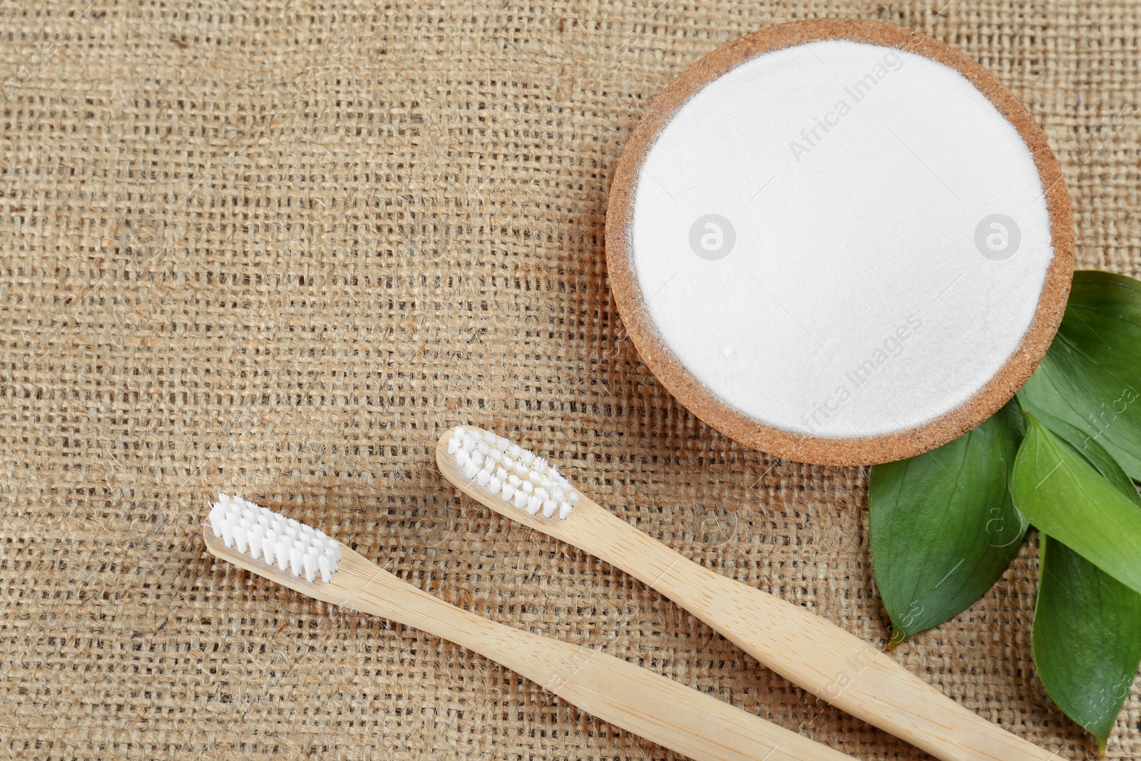 Photo of Bamboo toothbrushes and bowl of baking soda on sacking, flat lay