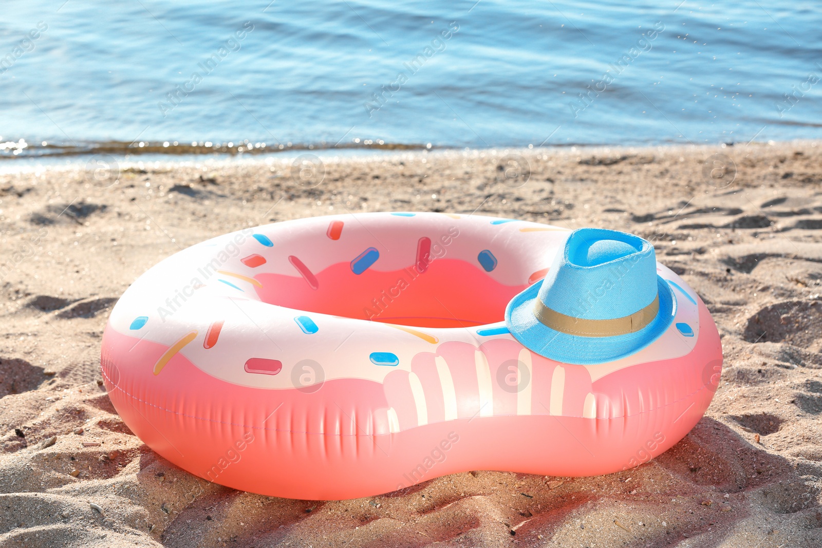 Photo of Inflatable donut and hat on sand near sea. Beach object