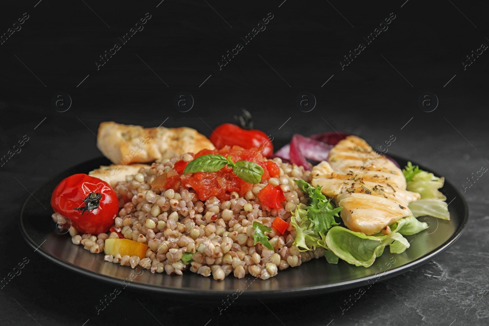 Photo of Tasty buckwheat porridge with meat and vegetables on black table