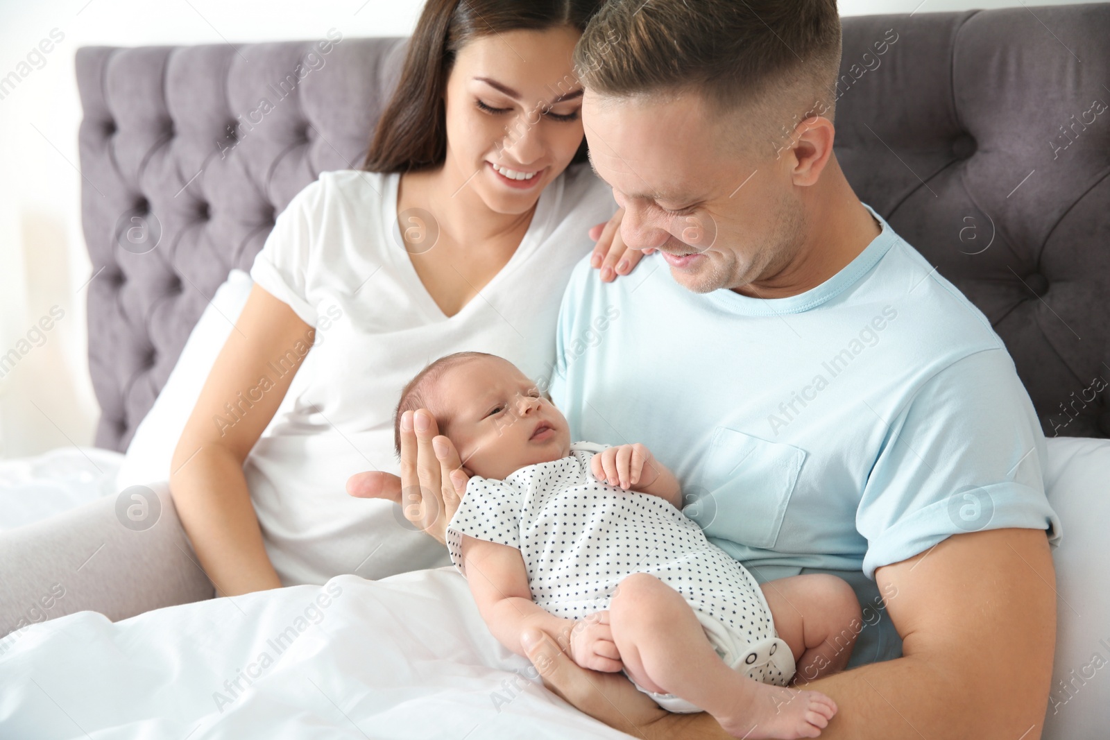 Photo of Happy couple with their newborn baby on bed