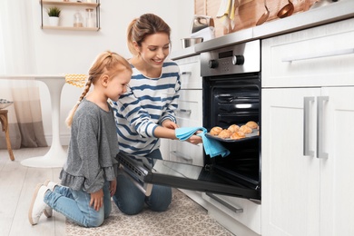 Mother and her daughter taking out cookies from oven in kitchen