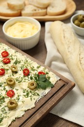 Photo of Fresh natural butter board with cut olives, pepper and bread on wooden table, closeup