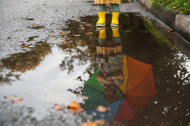 Little girl wearing yellow rubber boots standing in puddle outdoors, space for text