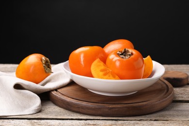 Delicious ripe persimmons on wooden table against black background