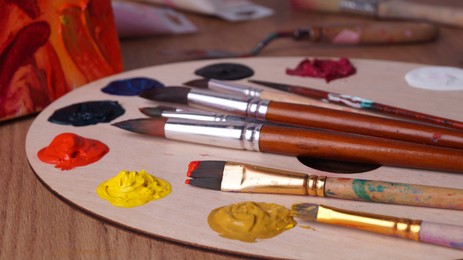 Photo of Artist's palette with many colorful paints and brushes on wooden table, closeup