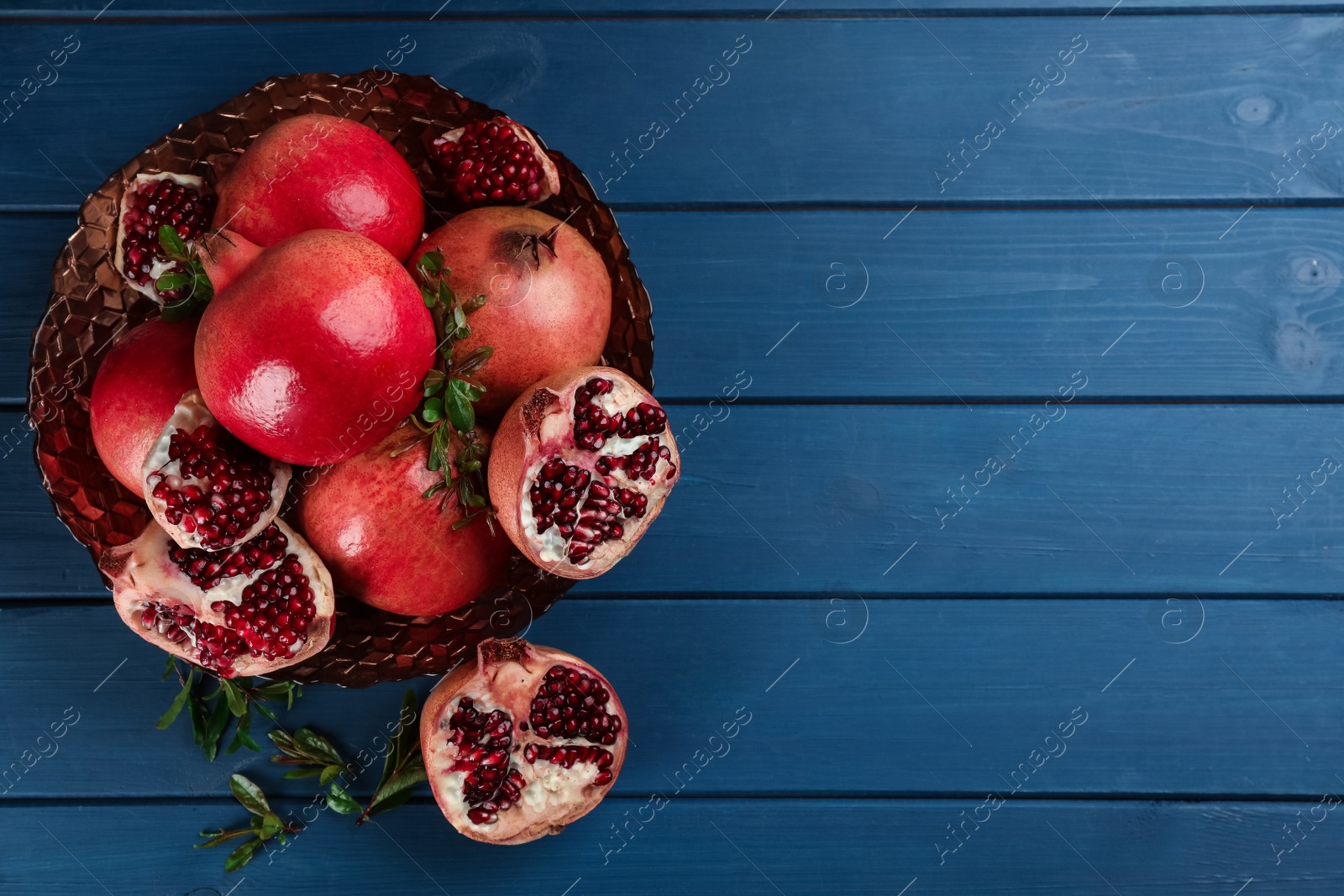 Photo of Delicious ripe pomegranates on blue wooden table, flat lay. Space for text