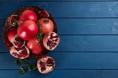 Photo of Delicious ripe pomegranates on blue wooden table, flat lay. Space for text