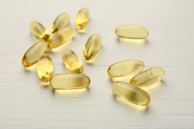 Yellow vitamin capsules on white wooden table, closeup