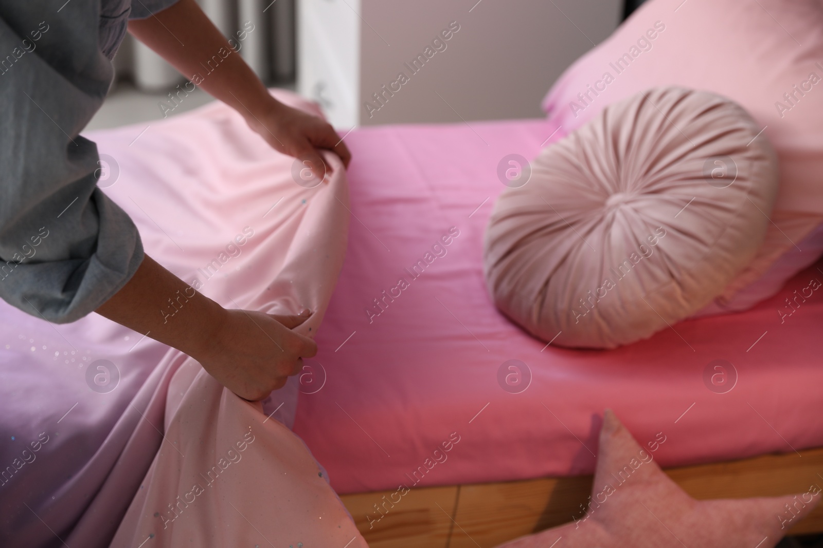 Photo of Woman making bed with new linens in children's room, closeup. Modern interior design