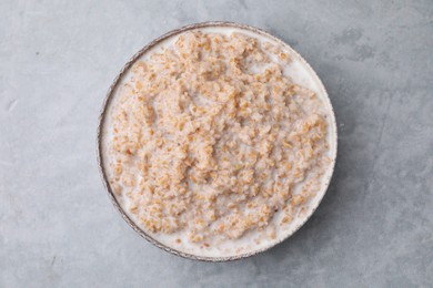 Photo of Tasty wheat porridge with milk in bowl on gray table, top view