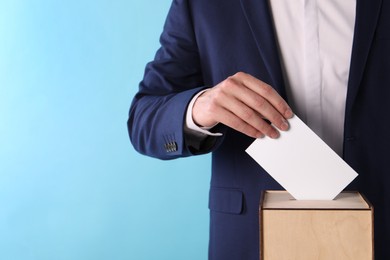 Photo of Man putting his vote into ballot box on light blue background, closeup. Space for text