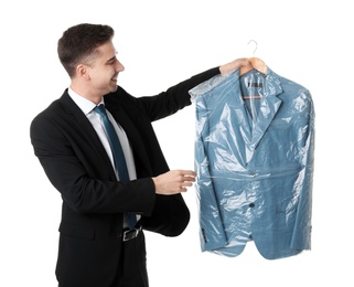 Photo of Young businessman holding hanger with jacket in plastic bag on white background. Dry-cleaning service