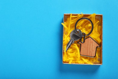 Photo of Key with trinket in shape of house and gift box on light blue background, top view. Space for text. Housewarming party