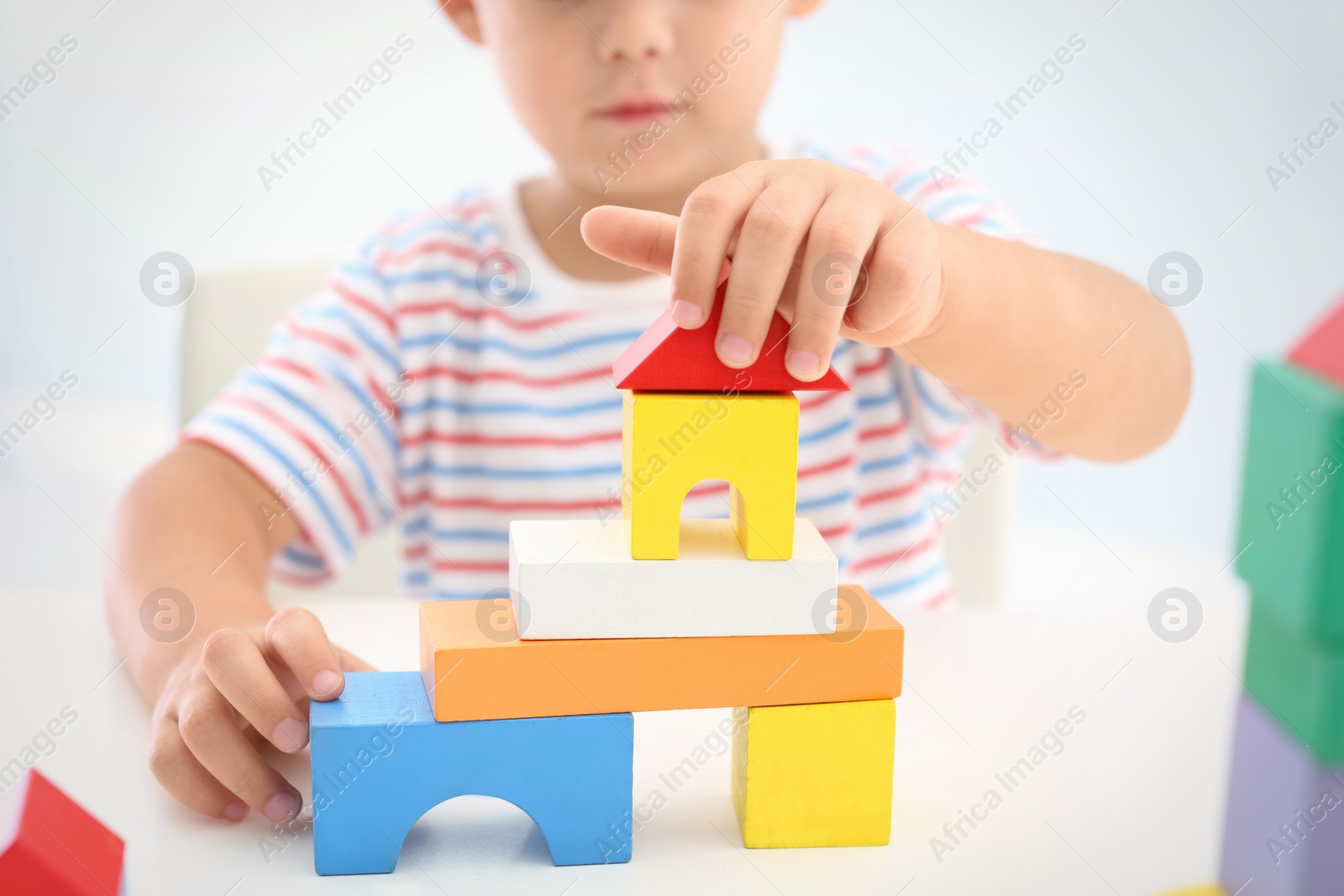 Photo of Little boy playing with colorful blocks at white table, closeup. Educational toy