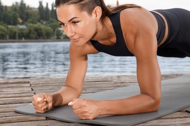 Young woman doing plank exercise on wooden pier near river, closeup