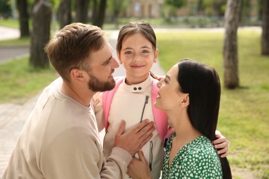 Photo of Parents hugging their little daughter before school outdoors