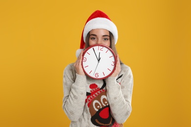 Photo of Woman in Santa hat with clock on yellow background. New Year countdown