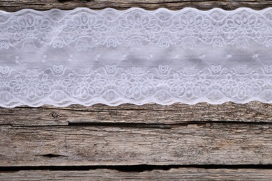 Photo of White lace on wooden table, top view. Space for text