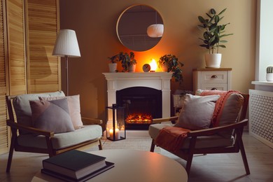 Photo of Stylish fireplace near comfortable armchairs and coffee table in cosy living room. Interior design