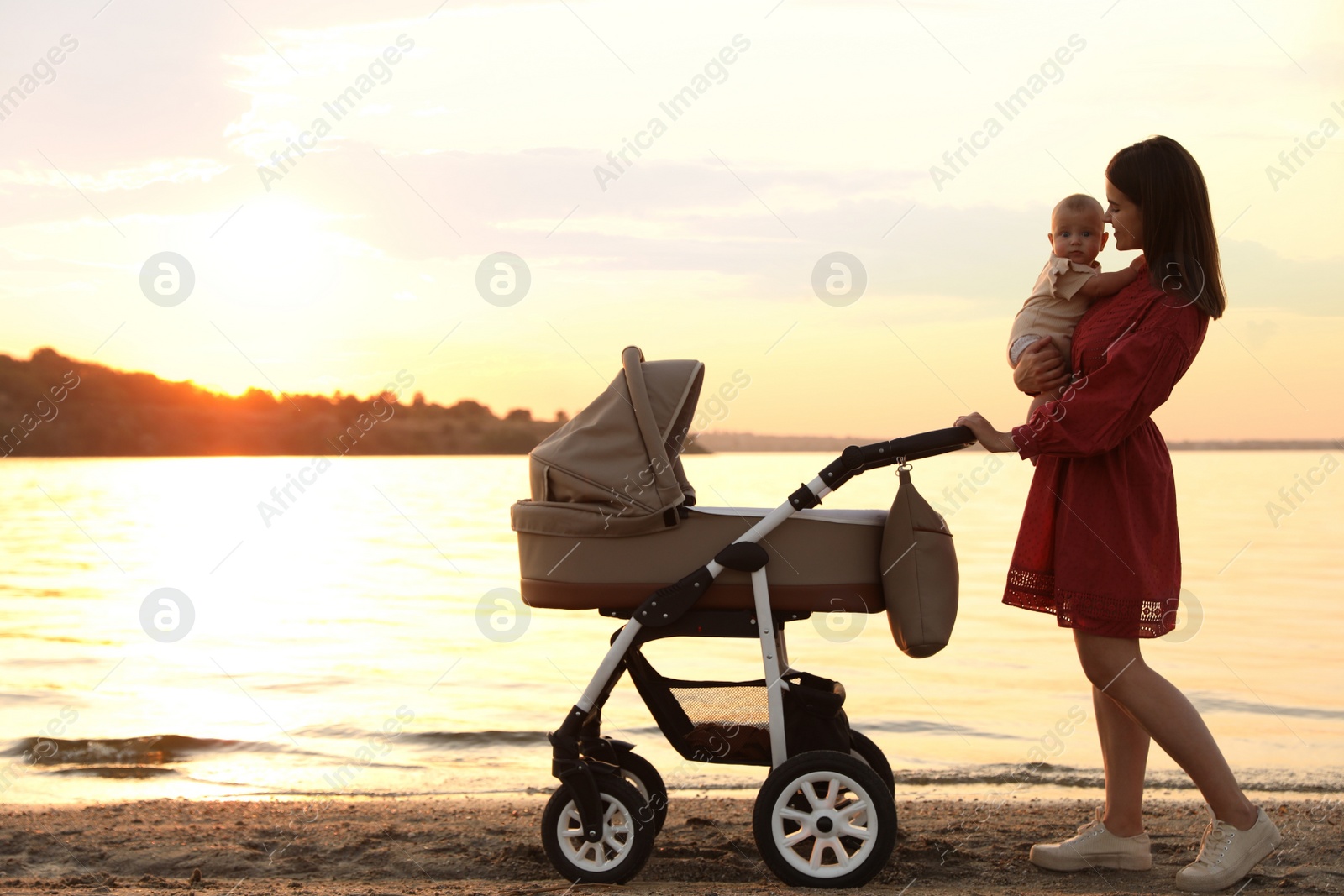 Photo of Happy mother with baby walking near river at sunset