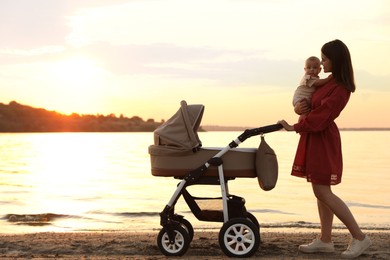 Happy mother with baby walking near river at sunset